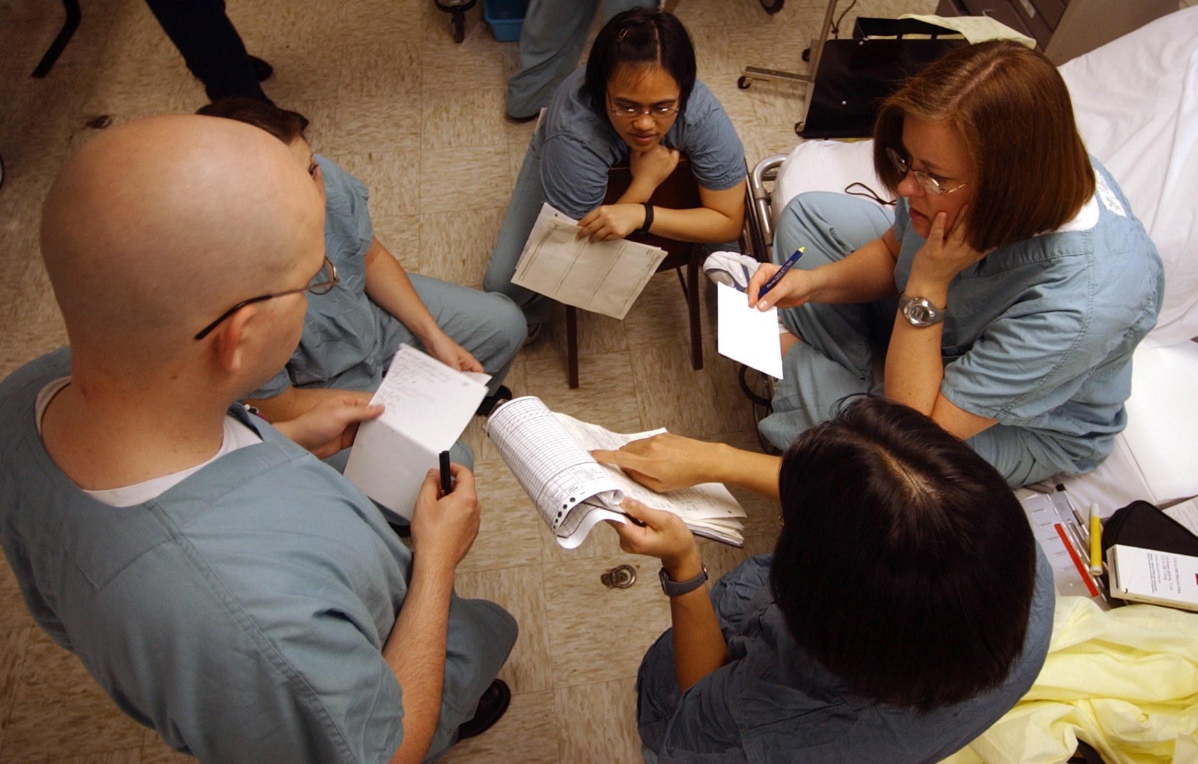 Nurses in scrubs reviewing patient notes during an ICU shift handoff aboard USNS Comfort